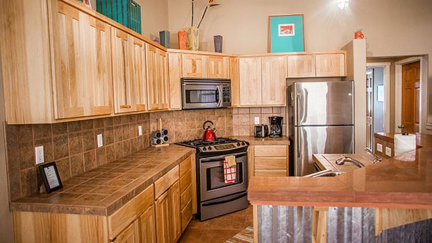 Small photo of a kitchen unit with lots of natural beige wood cabinets and storage, stainless steel appliances and breakfast counter at the Moab Springs Ranch property.