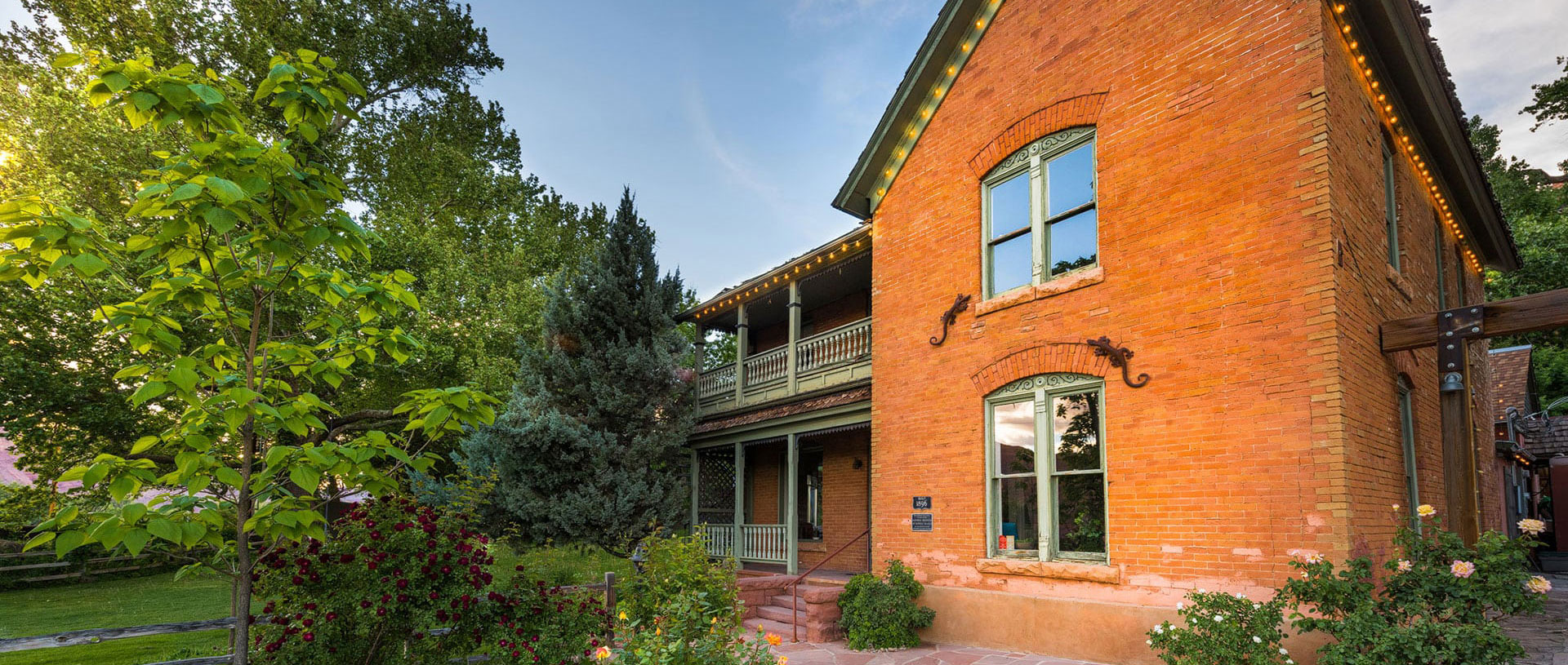 The historic ranch house on the Moab Springs property is a two storey faded red brick structure with a covered balcony on the upper floor overlooking lush vegetation.